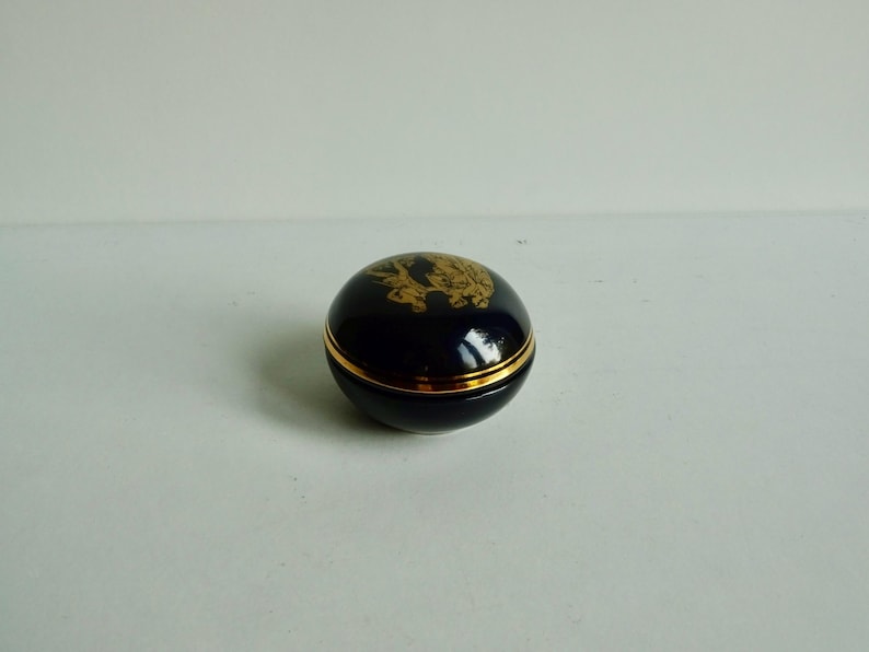May include: A small, round, blue and gold trinket box with a gold design on the lid.
