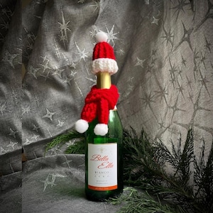 May include: A bottle of Bella Ella Bianco Zero Moscato wine with a red and white crocheted Santa hat and scarf.
