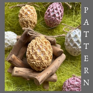 Könnte beinhalten: Häkelmuster für Ostereier in Rosa, Weiß und Gelb. Die Eier werden auf einem Holzständer präsentiert und von grünem Gras umgeben.