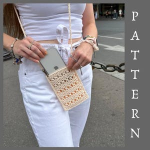 May include: A cream-colored crochet crossbody phone pouch featuring an openwork stitch pattern and a matching braided strap. The rectangular bag is designed to hold a smartphone and is worn over white clothing. The word PATTERN is written vertically.