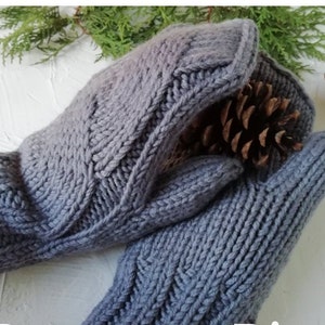 May include: A pair of grey knitted mittens featuring a textured cable knit pattern on the back of the hand. The mittens are constructed with a thick, chunky yarn and have a ribbed cuff design. The grey color is a solid, muted tone throughout.