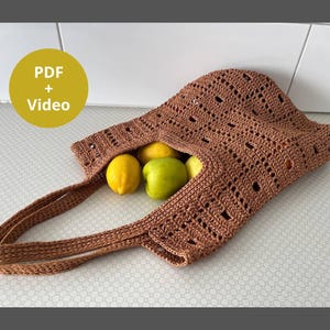 Può includere: Una borsa tote all'uncinetto marrone con un motivo traforato contenente due limoni gialli e una mela verde. Un grafico circolare giallo nell'angolo in alto a sinistra mostra il testo PDF + Video in lettere bianche.