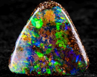 May include: A polished, triangular opal gemstone with a vibrant display of color. The stone features a mix of green, blue, orange, and brown hues, with a speckled, textured surface. The edges are a darker, speckled brown.