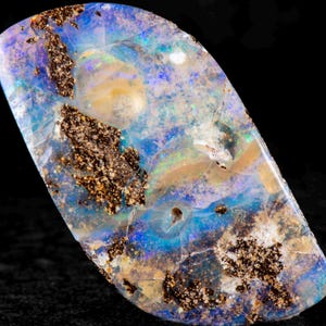 Könnte beinhalten: Ein polierter Opal-Edelstein mit einer lebendigen Farbgebung. Der Stein weist eine Mischung aus Blau, Grün und Gelb mit dunkelbraunen Einschlüssen auf. Der Opal ist vor einem schwarzen Hintergrund platziert.