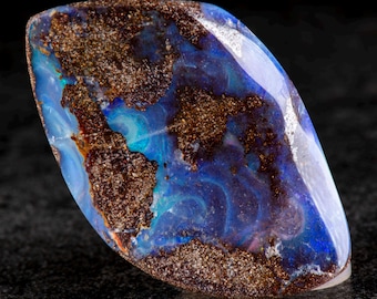 May include: A polished opal gemstone with a unique pattern of blue, brown, and white colors. The stone has a smooth, glossy surface and a natural, organic shape. The opal is a beautiful example of natural stone.
