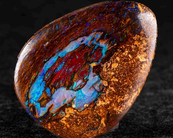 Puede incluir: Una piedra preciosa de ópalo pulido con una rica base marrón terroso. La piedra presenta vibrantes patrones internos de rojo, azul y blanco, creando un llamativo contraste visual. La superficie del ópalo es lisa y reflectante.