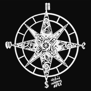 Puede incluir: Una brújula blanca con un diseño floral y el texto "wicked whimsy arts" en la parte inferior.