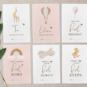 Pu&ograve; includere: Set di dieci schede di pietra miliare stampabili per una bambina. Le schede presentano uno schema di colori rosa e marrone con illustrazioni di una luna e stelle, una mongolfiera, un arcobaleno, un fiocco e un'anatra. Le schede hanno il testo che dice "Dieci mesi oggi", "Undici mesi oggi", "Oggi &egrave; il mio primo compleanno", "Oggi ho detto la mia prima parola", "Oggi ho fatto il mio primo taglio di capelli" e "Oggi ho fatto i miei primi passi".