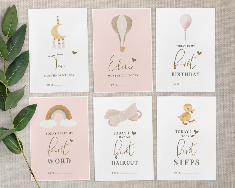Pu&ograve; includere: Set di dieci schede di pietra miliare stampabili per una bambina. Le schede presentano uno schema di colori rosa e marrone con illustrazioni di una luna e stelle, una mongolfiera, un arcobaleno, un fiocco e un'anatra. Le schede hanno il testo che dice "Dieci mesi oggi", "Undici mesi oggi", "Oggi &egrave; il mio primo compleanno", "Oggi ho detto la mia prima parola", "Oggi ho fatto il mio primo taglio di capelli" e "Oggi ho fatto i miei primi passi".