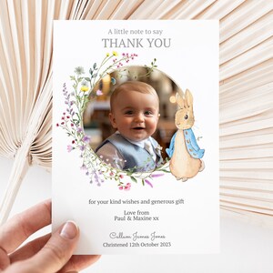 May include: A thank you card with a watercolour floral wreath and a photo of a baby boy. The card also features a cartoon illustration of Peter Rabbit. The text on the card reads "A little note to say THANK YOU for your kind wishes and generous gift. Love from Paul & Maxine xx. Calluen James Jones Christened 12th October 2023."