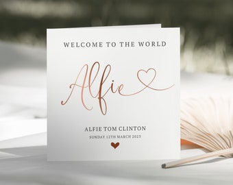 Puede incluir: Una tarjeta blanca con el texto "Bienvenido al mundo" y el nombre "Alfie" escrito en cursiva con un corazón de color cobre. El texto "Alfie Tom Clinton" y "Domingo 12 de marzo de 2023" también está escrito en la tarjeta.