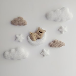 Peut inclure: Décoration murale de chambre d'enfant avec un ours en peluche sur un croissant de lune blanc, entouré d'étoiles blanches et de nuages ​​duveteux beiges et blancs. L'ensemble est conçu pour une chambre de bébé.