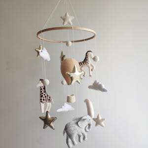 Op de afbeelding: Een houten babymobiel met een neutraal kleurenschema. Het heeft een luchtballon, een giraffe, een zebra, een olifant, wolken en sterren. De mobiel is perfect voor een kinderkamer of babykamer.