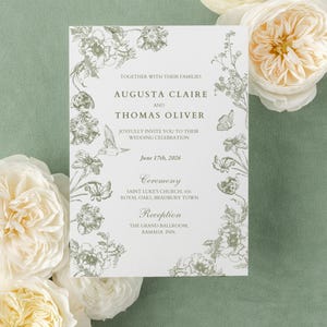 May include: A wedding invitation with floral illustrations in a soft green hue. The invitation features the names Augusta Claire and Thomas Oliver, along with the wedding date and location. White flowers surround the invitation on a light green background.