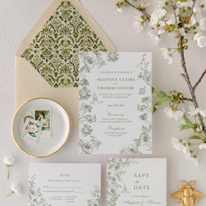 May include: Wedding invitation suite with floral design in green and white. Includes invitation, RSVP card, and save-the-date card. An envelope with a patterned interior and a decorative bee are also present. The invitation reads "Augusta Claire and Thomas Oliver".