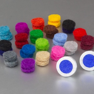 Könnte beinhalten: Eine Sammlung farbenfroher Filzkreise in verschiedenen Farbtönen, darunter Blau, Rot, Gelb und Lila. Zwei weiße und blaue kreisförmige Objekte befinden sich im Vordergrund. Die Filzkreise sind paarweise gestapelt.