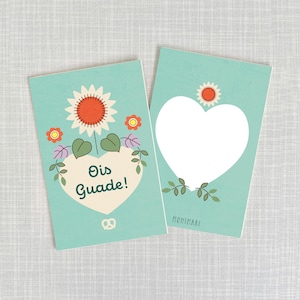 Könnte beinhalten: Zwei türkisfarbene Karten mit einem floralen Design. Die erste Karte hat ein Herz mit dem Text "Oi's Guade!" darin. Die zweite Karte hat ein leeres Herz.