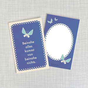 Può includere: Due carte blu con bordi bianchi a festoni e illustrazioni di farfalle. La carta a sinistra ha il testo "Beinahe alles kommt von beinahe nichts." La carta a destra ha un cerchio bianco al centro.
