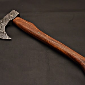May include: A handcrafted axe with a patterned steel blade and a dark wooden handle. The axe head features a unique swirling pattern. The handle is a rich brown color, with a smooth, polished finish. The axe is a tool for woodworking or outdoor activities.