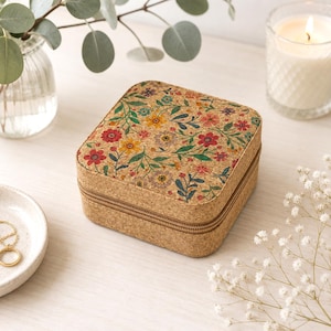 Könnte beinhalten: Eine quadratische Schmuckschatulle aus Kork mit einem bunten Blumenmuster aus roten, gelben und blauen Blüten sowie grünen Blättern. Die Schatulle hat eine beige, strukturierte Korkoberfläche und einen Reißverschluss an den Seiten.