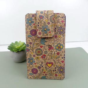 Könnte beinhalten: Eine rechteckige Handyhülle mit Klappverschluss, verziert mit einem Blumenmuster in Blau, Gelb und Rot auf Korkbasis. Die Hülle hat eine strukturierte Oberfläche und einen dunklen Rand.