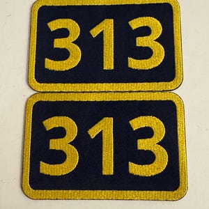 May include: Two black fabric patches with a gold border and the number 313 embroidered in gold.
