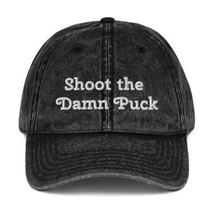 以下が含まれることがあります： 「Shoot the Damn Puck」という白い刺繍が施された黒いビンテージベースボールキャップ。