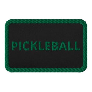 Puede incluir: Un parche rectangular negro con un borde verde y la palabra "PICKLEBALL" bordada en verde.