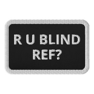 May include: A rectangular patch with a black background and white embroidered text that reads "R U BLIND REF?". The patch has a white border with a stitched texture.