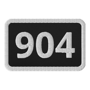 Könnte beinhalten: Ein schwarzer rechteckiger Patch mit einer weißen gestickten Nummer "904" darauf.