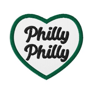 May include: A white heart-shaped patch with a green border. The patch has the text "Philly Philly" in black cursive lettering.