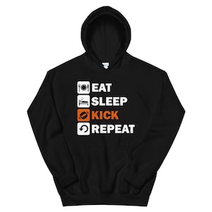 May include: Black hooded sweatshirt with the words "EAT SLEEP KICK REPEAT" in white and orange. The design includes icons of a plate, bed, football, and a circular arrow. The sweatshirt has a front pocket and a hood.