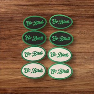 May include: Eight oval-shaped iron-on patches with a green outline and white or black background. The text "Go Birds" is written in green cursive lettering on each patch.