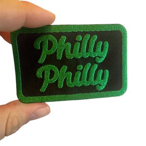 Op de afbeelding: Groen geborduurd patch met de tekst "Philly Philly" in een zwart vierkant met een groene rand.