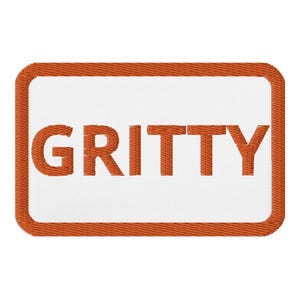 Op de afbeelding: Oranje geborduurde patch met een witte achtergrond en het woord "GRITTY" in oranje.