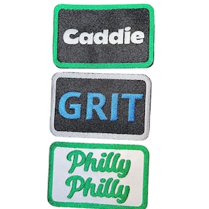 May include: Three embroidered patches with black backgrounds and green borders. The top patch says "Caddie" in white text. The middle patch says "GRIT" in blue text. The bottom patch says "Philly Philly" in green text.