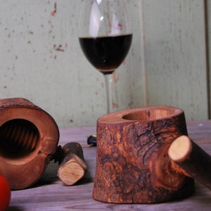 May include: Two wooden nutcrackers made from tree bark. The nutcracker on the left is open, showing the internal mechanism. The nutcracker on the right is closed and has a wooden handle.