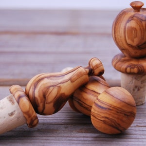 Può includere: Tre tappi per bottiglia in legno con fondo in sughero. I tappi sono scolpiti a forma di pera, fungo e sfera rotonda. Il legno è di colore marrone chiaro con venature marroni scure.