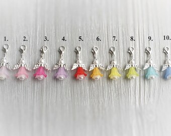 May include: Eleven angel charms with silver clips and wings. The charms are made of plastic and have a bell shape. The colors are pink, red, purple, orange, yellow, light blue, dark blue, and black.