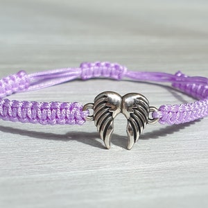 Op de afbeelding: Een paars gevlochten armband met een zilveren engelenvleugelbedel.