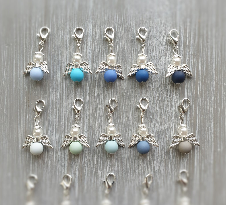 May include: Twelve silver angel charms with different colored beads. The beads are light blue, turquoise, dark blue, gray, light green, and brown.