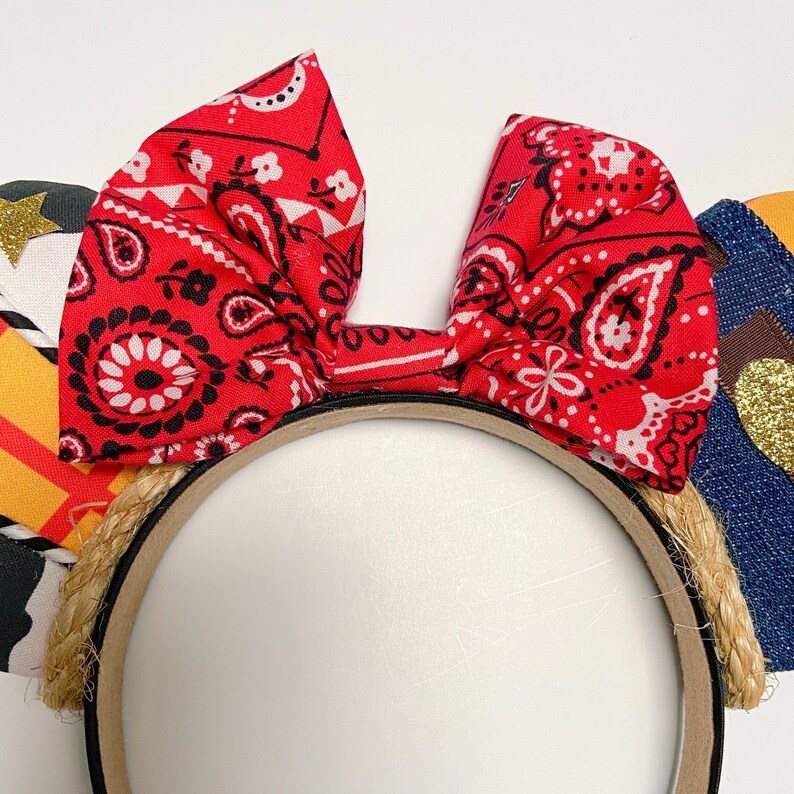 Peut inclure: Un serre-t&ecirc;te avec un n&oelig;ud en bandana rouge et blanc et une bordure en corde brune. Le serre-t&ecirc;te est en tissu et pr&eacute;sente un motif de bandana rouge et blanc.