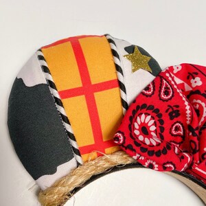 Peut inclure: Une paire d'oreilles de Mickey Mouse faites &agrave; la main avec un bandana rouge et noir, un tissu &agrave; carreaux jaune et rouge et un tissu noir et blanc avec une &eacute;toile. Les oreilles sont attach&eacute;es &agrave; un bandeau marron.