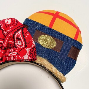 Peut inclure: Une paire d'oreilles de Minnie Mouse faites &agrave; la main avec un bandana rouge &agrave; motif paisley blanc et un chapeau de cowboy en denim bleu et tissu jaune avec un accent de paillettes dor&eacute;es.