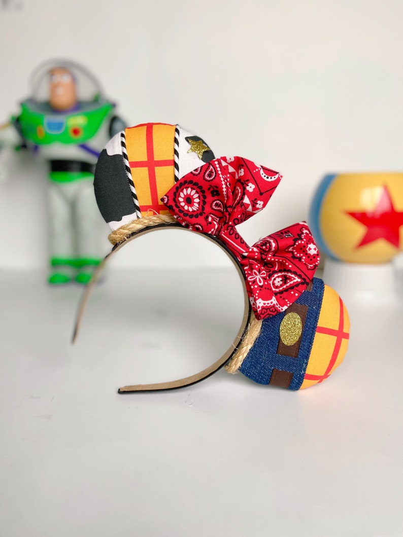 Peut inclure: Une paire d'oreilles de Minnie Mouse faites &agrave; la main sur le th&egrave;me de Disney avec un bandana rouge, un motif en tissu denim et jaune et un bandeau en corde marron.