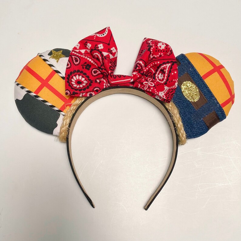 Peut inclure: Oreilles de Mickey Mouse en tissu rouge, jaune et bleu avec un n&oelig;ud bandana. Les oreilles sont d&eacute;cor&eacute;es d'un motif patchwork.