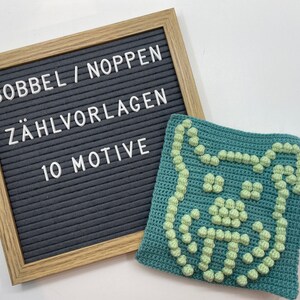 Peut inclure: Un tableau d'affichage en lettres gris avec le texte "BOBBEL / NOPPEN ZÄHLVORLAGEN 10 MOTIVE" et un carré crocheté vert avec un motif de points bouclés vert clair.