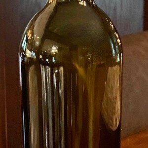 May include: A dark green glass bottle with a cork stopper. The bottle has a rounded body and a narrow neck. A copper-coloured ring is at the bottom. The cork has the word "Pinot" printed on it.