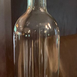 May include: A clear glass bottle with a cork stopper. The bottle is decorated with a band of clear rhinestones near the top and bottom. The cork has the word "Principessa" printed on it.