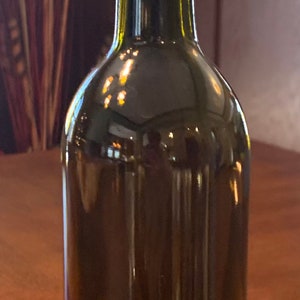 May include: A dark green glass bottle with a cork stopper. The bottle is decorated with two bands of clear rhinestones. The bottle is likely a decorative piece or a repurposed item.